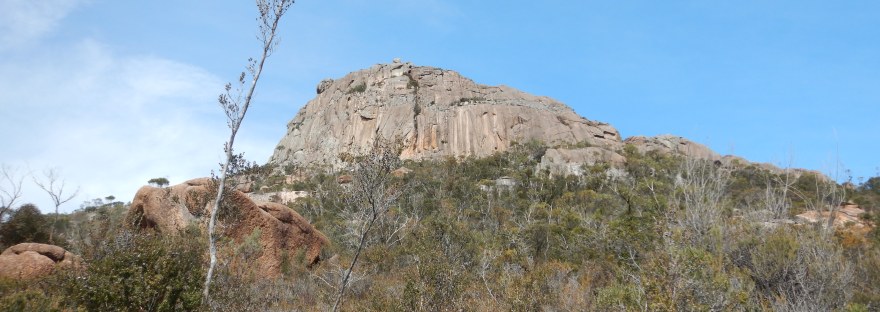 Mt Amos, a rocky outcrop, juts sharply out from scrubby bushes. White streaks are formed naturally by water running down the rocks over time.